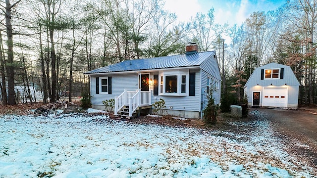 view of front of house featuring driveway, a detached garage, a chimney, metal roof, and an outbuilding