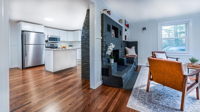 kitchen with dark wood-type flooring, white cabinets, wooden walls, a kitchen island, and stainless steel appliances