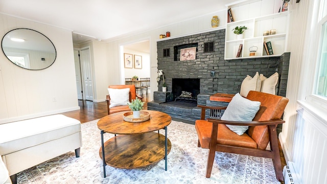 living room featuring hardwood / wood-style flooring, ornamental molding, baseboard heating, and a brick fireplace