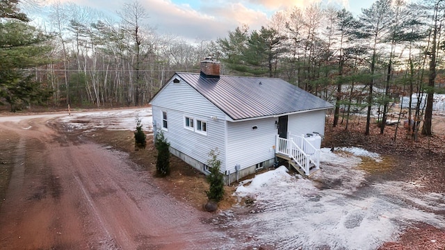 exterior space featuring dirt driveway, metal roof, and a chimney