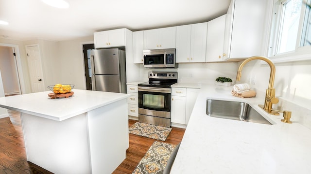 kitchen with dark wood finished floors, appliances with stainless steel finishes, a center island, white cabinetry, and a sink