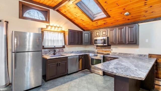 kitchen with sink, kitchen peninsula, lofted ceiling with skylight, dark brown cabinets, and appliances with stainless steel finishes