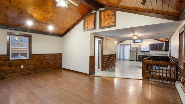 interior space with light wood-type flooring, wood ceiling, wooden walls, a baseboard radiator, and beamed ceiling