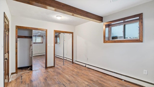 unfurnished bedroom with wood-type flooring, baseboard heating, and two closets