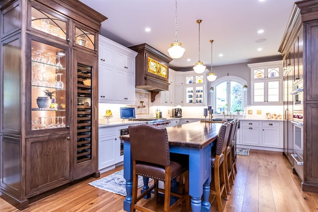 kitchen with a kitchen island, decorative light fixtures, a breakfast bar, white cabinets, and light wood-type flooring