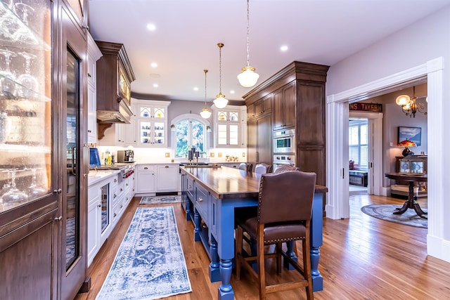 kitchen featuring a kitchen bar, a kitchen island, decorative light fixtures, light hardwood / wood-style floors, and white cabinetry