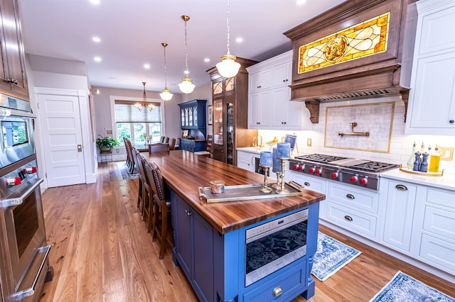 kitchen with appliances with stainless steel finishes, premium range hood, blue cabinetry, white cabinetry, and butcher block counters