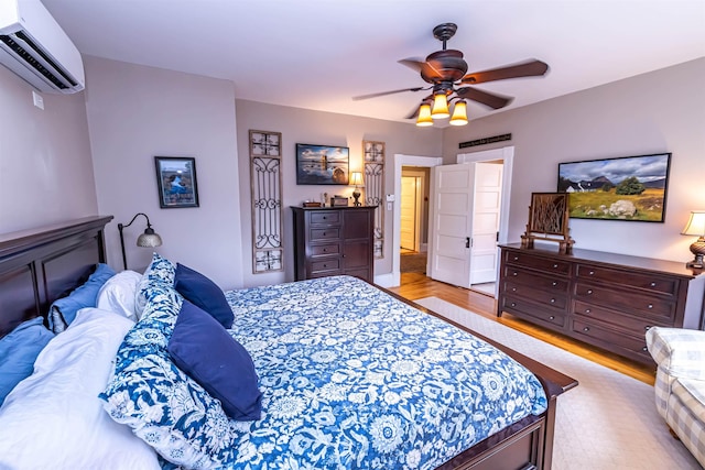 bedroom with light hardwood / wood-style floors, a wall unit AC, and ceiling fan