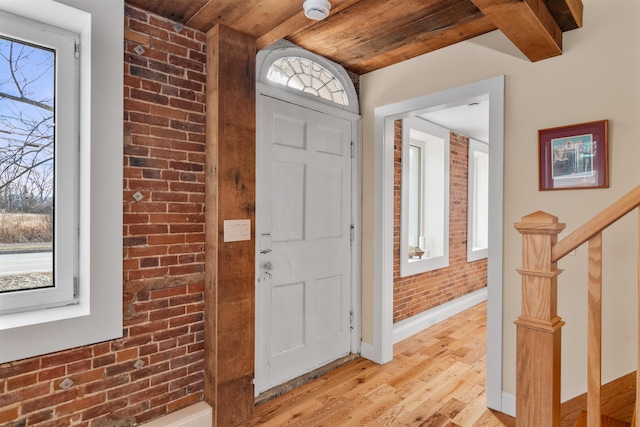 foyer entrance featuring a healthy amount of sunlight, wooden ceiling, beam ceiling, and brick wall