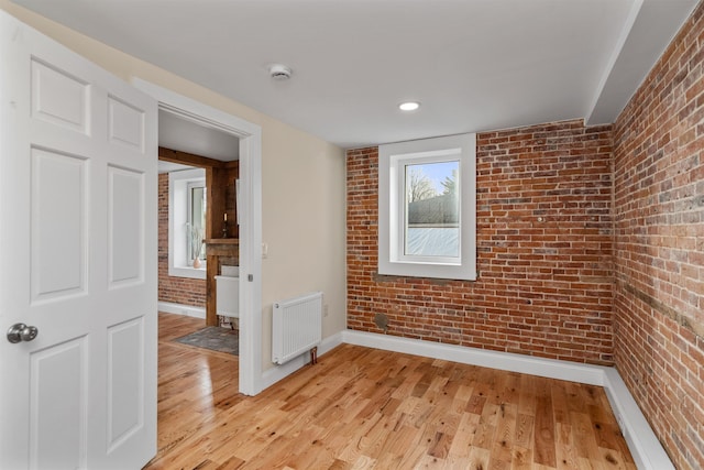 empty room featuring light hardwood / wood-style floors, radiator heating unit, and brick wall