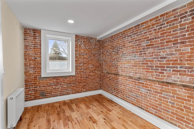 empty room with radiator heating unit, brick wall, and light wood-type flooring