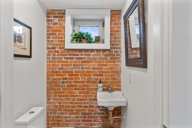 bathroom featuring brick wall and toilet