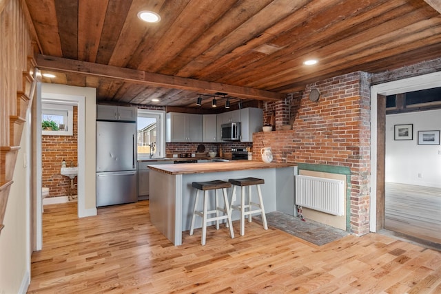 kitchen featuring rail lighting, kitchen peninsula, gray cabinets, a breakfast bar, and appliances with stainless steel finishes