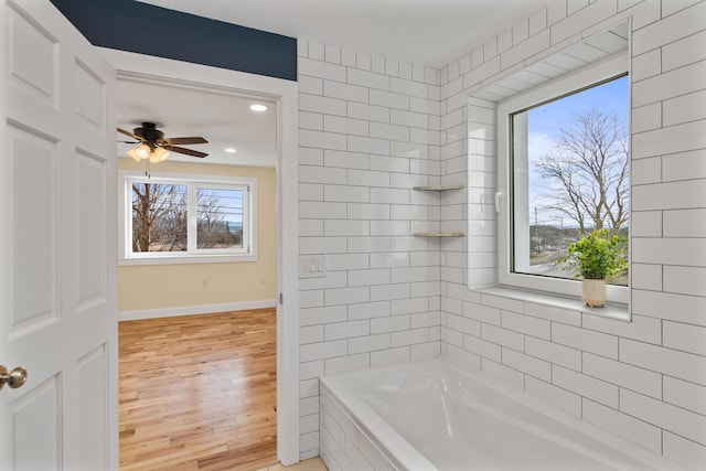 bathroom featuring hardwood / wood-style floors, ceiling fan, tiled tub, and a wealth of natural light