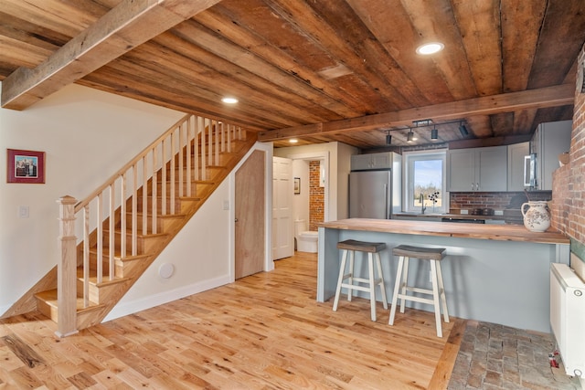 kitchen with kitchen peninsula, track lighting, gray cabinetry, butcher block counters, and a breakfast bar area