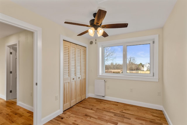 unfurnished bedroom with ceiling fan, light wood-type flooring, radiator heating unit, and a closet