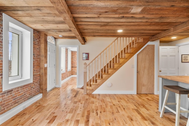 foyer with beamed ceiling, light wood-type flooring, wood ceiling, and brick wall