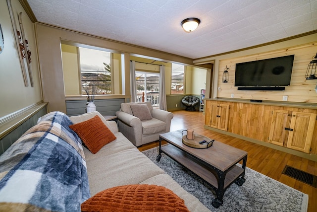 living room featuring wooden walls, light hardwood / wood-style floors, and ornamental molding