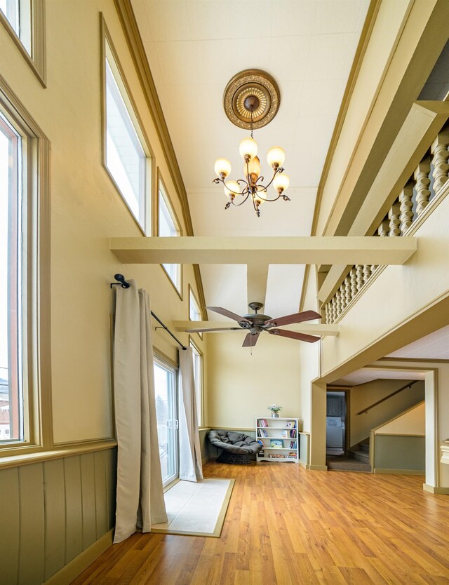 unfurnished living room with wood-type flooring, ceiling fan with notable chandelier, and a high ceiling