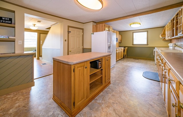 kitchen featuring white fridge with ice dispenser, a kitchen island, stove, and ornamental molding