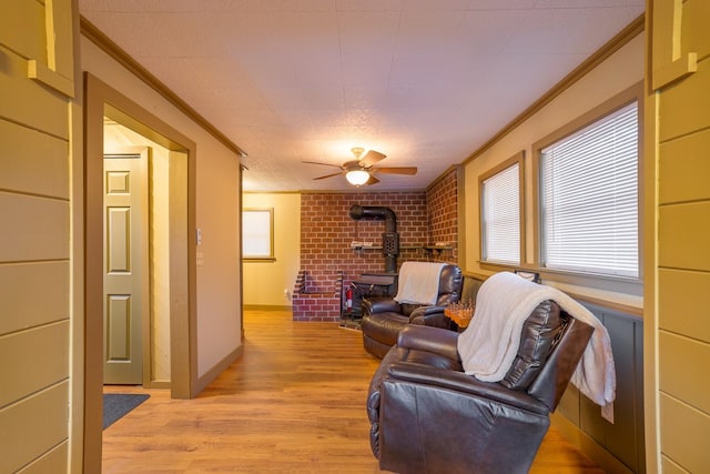 living room with a wood stove, crown molding, ceiling fan, light wood-type flooring, and brick wall