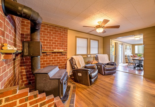 living room with a wood stove, ceiling fan, crown molding, and wood-type flooring