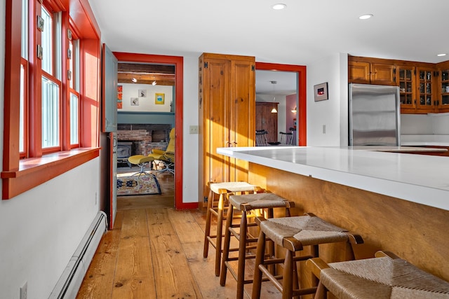 kitchen with a breakfast bar, a fireplace, stainless steel fridge, baseboard heating, and light hardwood / wood-style flooring