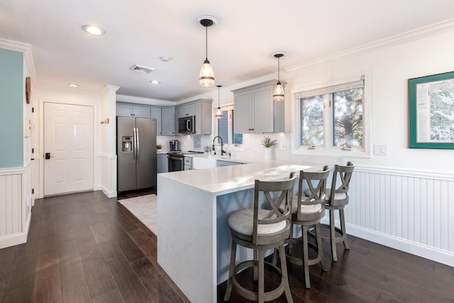 kitchen featuring a kitchen breakfast bar, crown molding, hanging light fixtures, dark hardwood / wood-style floors, and appliances with stainless steel finishes