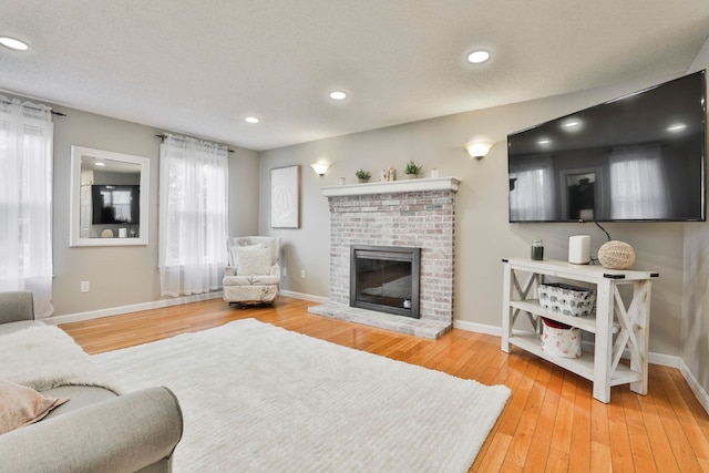 living room featuring wood-type flooring, a textured ceiling, and a brick fireplace