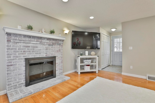 living room featuring hardwood / wood-style flooring, a textured ceiling, and a brick fireplace