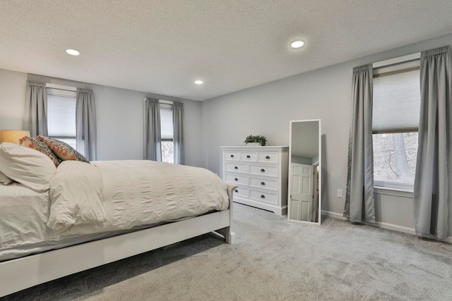 bedroom featuring a textured ceiling, light colored carpet, and multiple windows