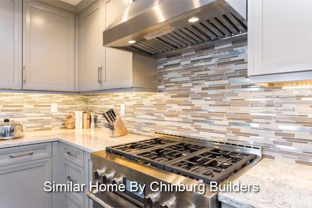 kitchen featuring tasteful backsplash, stove, wall chimney exhaust hood, and light stone counters