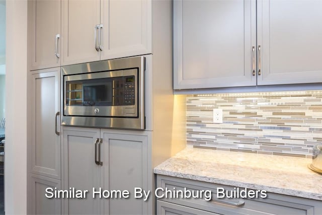 kitchen featuring stainless steel microwave, gray cabinetry, decorative backsplash, and light stone counters