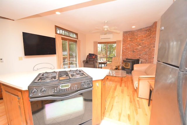 kitchen featuring a wood stove, an AC wall unit, ceiling fan, stainless steel fridge, and black range with gas cooktop