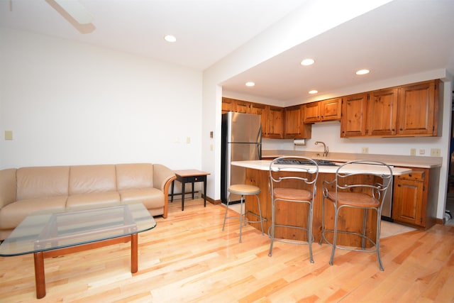 kitchen featuring stainless steel refrigerator, sink, a center island, light hardwood / wood-style floors, and a breakfast bar area