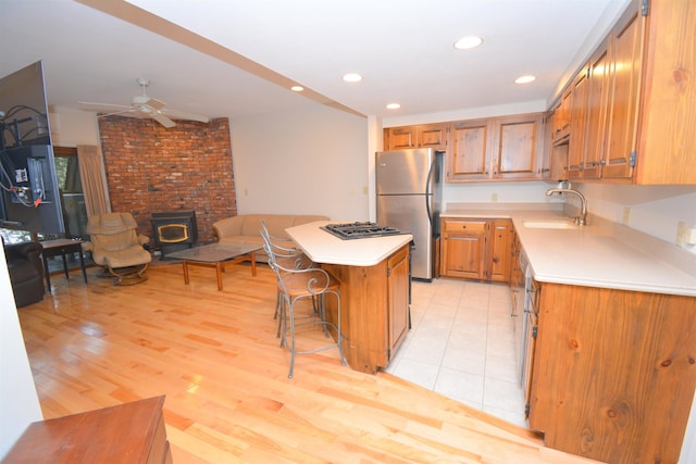 kitchen with a wood stove, ceiling fan, sink, stainless steel appliances, and a breakfast bar area