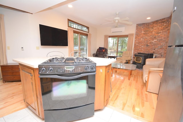 kitchen with black range with gas cooktop, ceiling fan, a wall mounted AC, a wood stove, and light tile patterned flooring