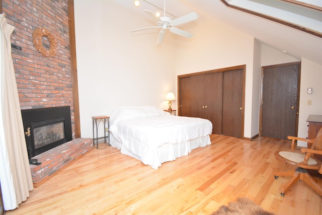 bedroom with ceiling fan, light hardwood / wood-style floors, vaulted ceiling, and a brick fireplace