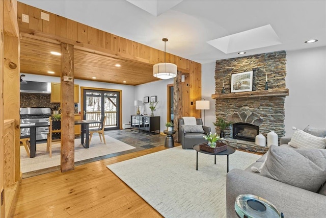 living room featuring hardwood / wood-style flooring, a stone fireplace, and a skylight