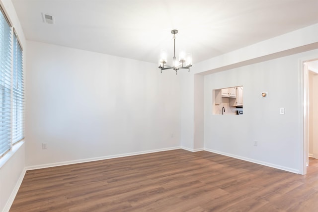 empty room with dark hardwood / wood-style flooring and a notable chandelier