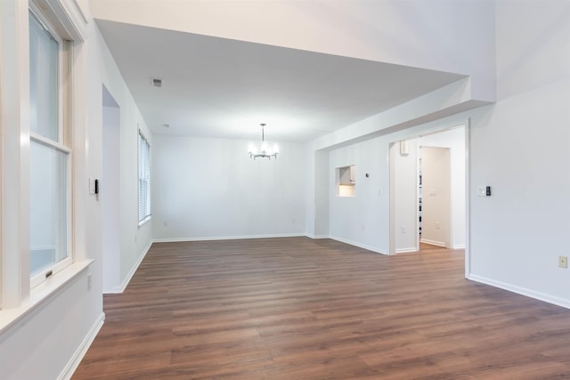 empty room with dark hardwood / wood-style floors and an inviting chandelier