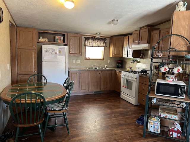 kitchen featuring dark hardwood / wood-style flooring, dark stone counters, white appliances, a textured ceiling, and sink