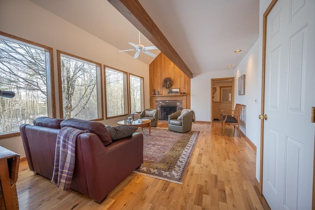 living room with ceiling fan, a fireplace, lofted ceiling with beams, and light wood-type flooring