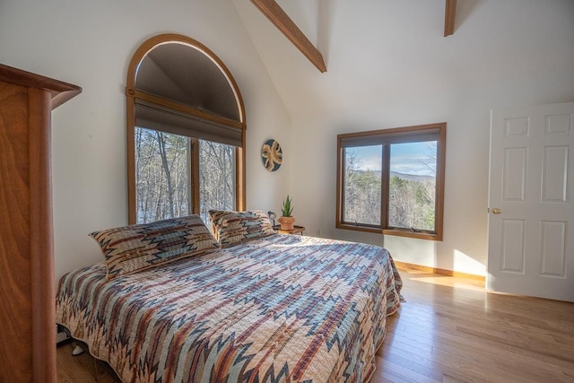 bedroom with beam ceiling, high vaulted ceiling, and light hardwood / wood-style flooring