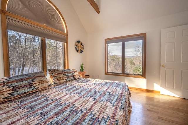 unfurnished bedroom featuring multiple windows, beamed ceiling, light hardwood / wood-style floors, and high vaulted ceiling