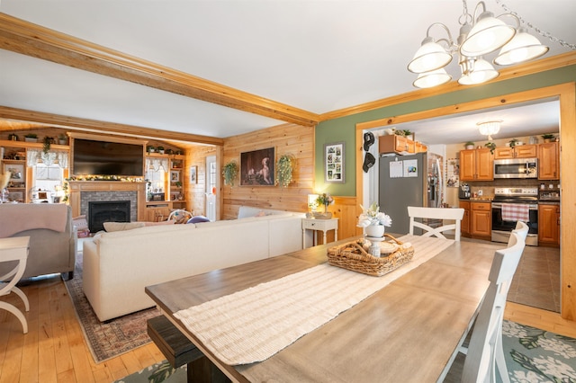 dining area with crown molding, wood walls, a chandelier, light hardwood / wood-style floors, and a fireplace