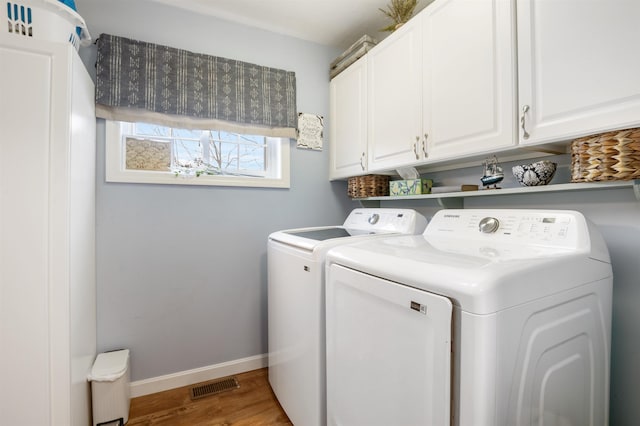 laundry area featuring washer and clothes dryer, light hardwood / wood-style floors, and cabinets