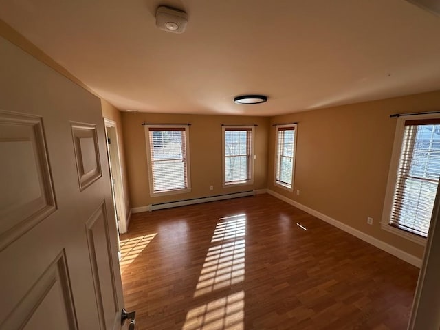 empty room featuring baseboards, a baseboard heating unit, and wood finished floors