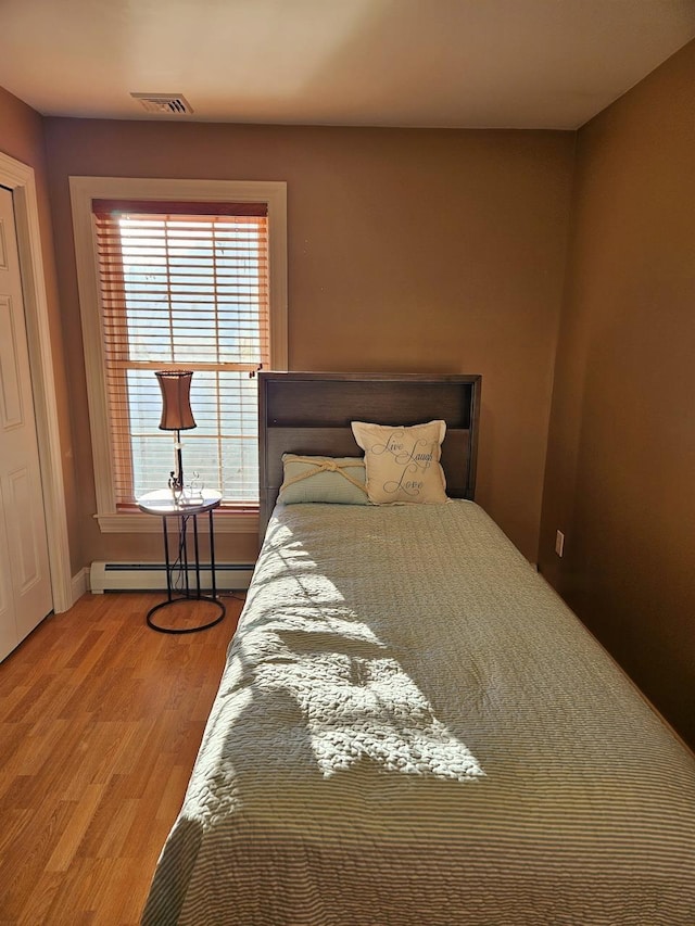 bedroom featuring baseboard heating, wood finished floors, visible vents, and baseboards