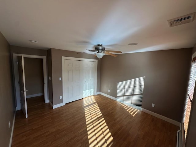 unfurnished bedroom with ceiling fan, a closet, dark hardwood / wood-style floors, and a baseboard heating unit